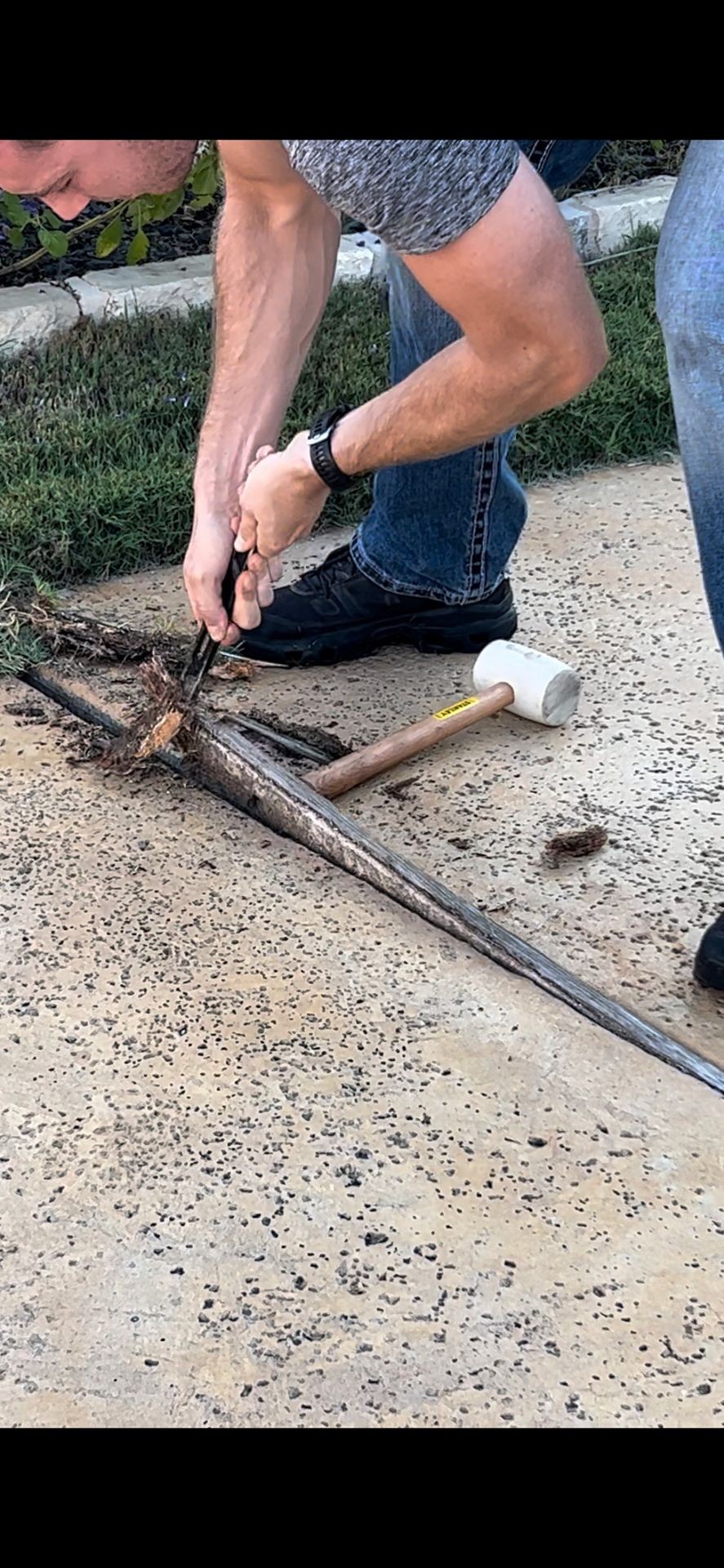 Removing rotted wood from Austin driveway expansion joint using pry bar and mallet during professional concrete joint replacement